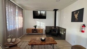 Ein Wohnzimmer mit einem Couchtisch aus Holz, einem an der Wand montierten Fernseher, einem Kamin und einem Feuerlöscher.