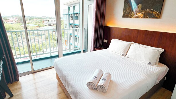 A hotel room with a large bed, a painting on the wall, and a balcony with a view of buildings and greenery. - EMART HOTEL RIAM SDN BHD (Miri)