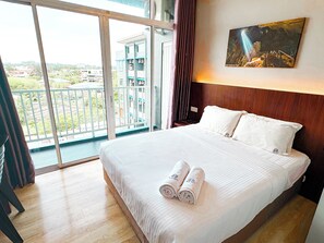 A hotel room with a large bed, a painting on the wall, and a balcony with a view of buildings and greenery. - EMART HOTEL RIAM SDN BHD (Miri)