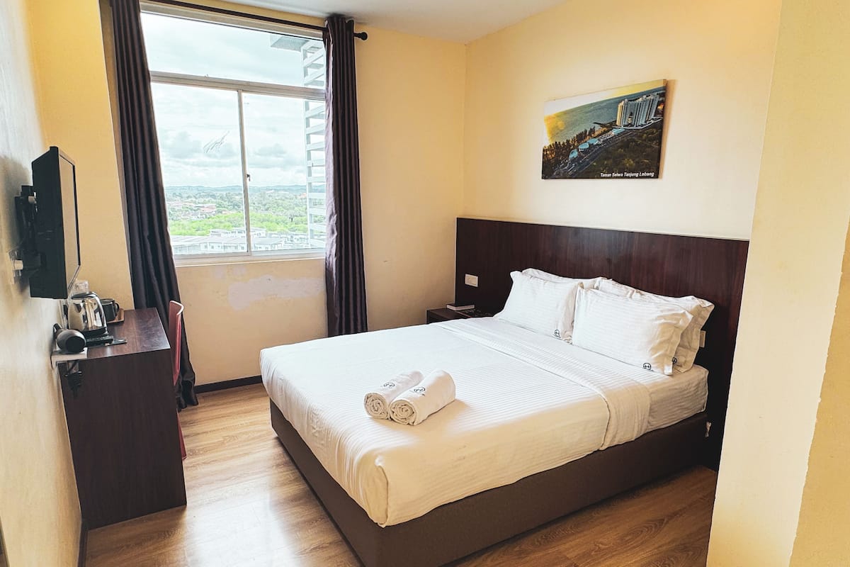 Habitación de hotel con una cama grande, una mesita de noche con tetera, una lámpara y un cuadro en la pared.