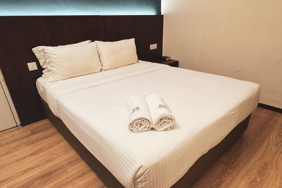 Una cama bien hecha con cabecera, dos almohadas y dos toallas enrolladas sobre la cama.