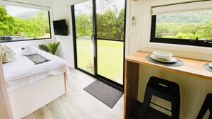 Une chambre moderne équipée d’un lit, d’un petit bureau et d’une grande porte-fenêtre coulissante donnant sur un jardin.