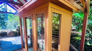 Une structure en bois dotée de portes et de fenêtres en verre, entourée de gravier et de verdure.