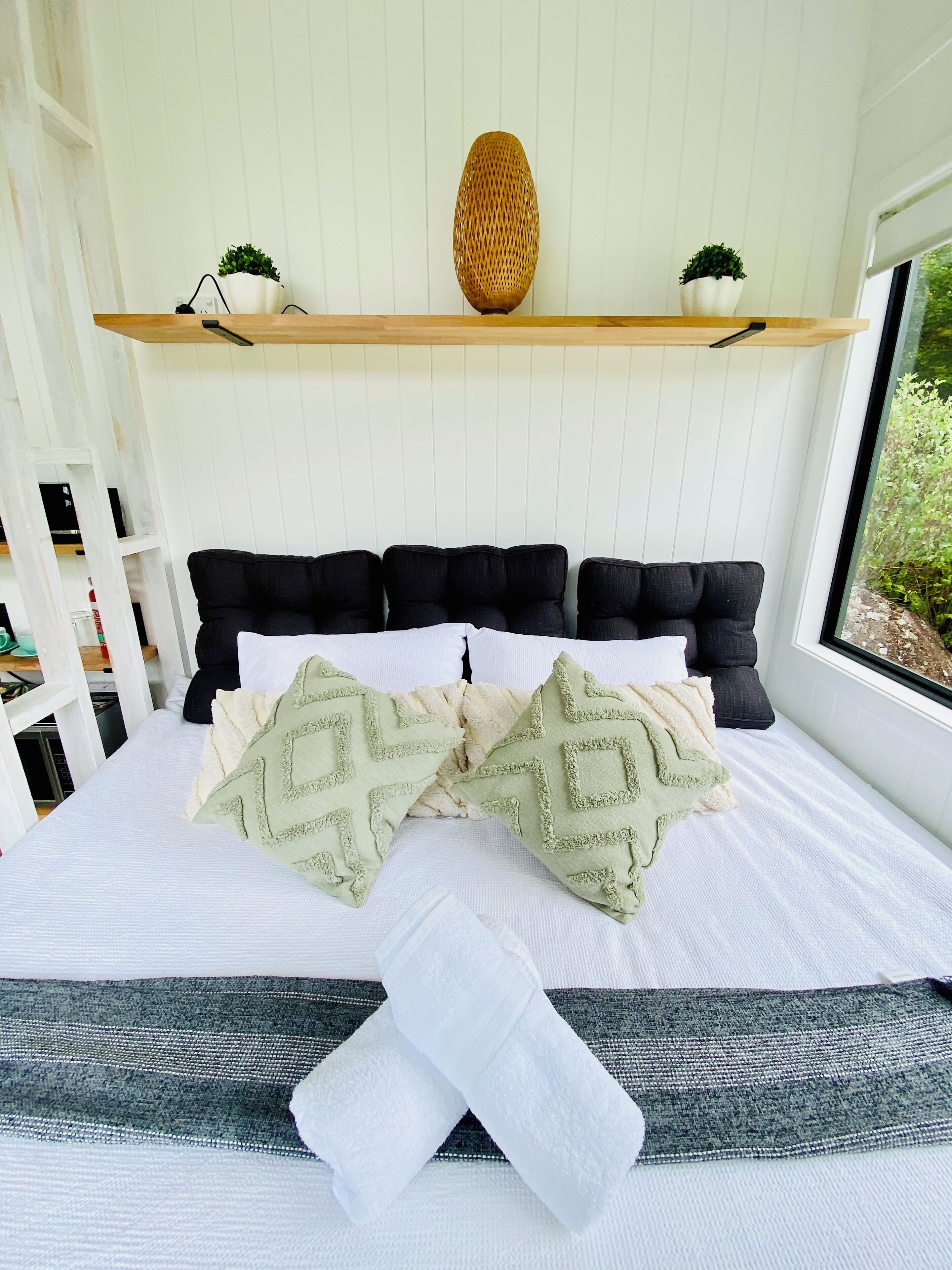 Un letto ben rifatto con cuscini decorati, un comodino e una finestra con vista sul verde.