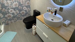 A modern bathroom with a floral wallpaper, a round mirror, a sink with a soap dispenser, and a toilet.