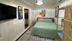 A bedroom with a bed, a TV, a chandelier, and artwork on the walls.