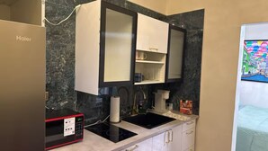 A compact kitchen with a black induction cooktop, a white sink, and a white cabinet with a mirror above it.