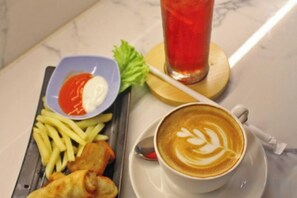 Un plato con papas fritas, alimentos fritos y una taza de café con arte latte sobre una mesa de mármol.