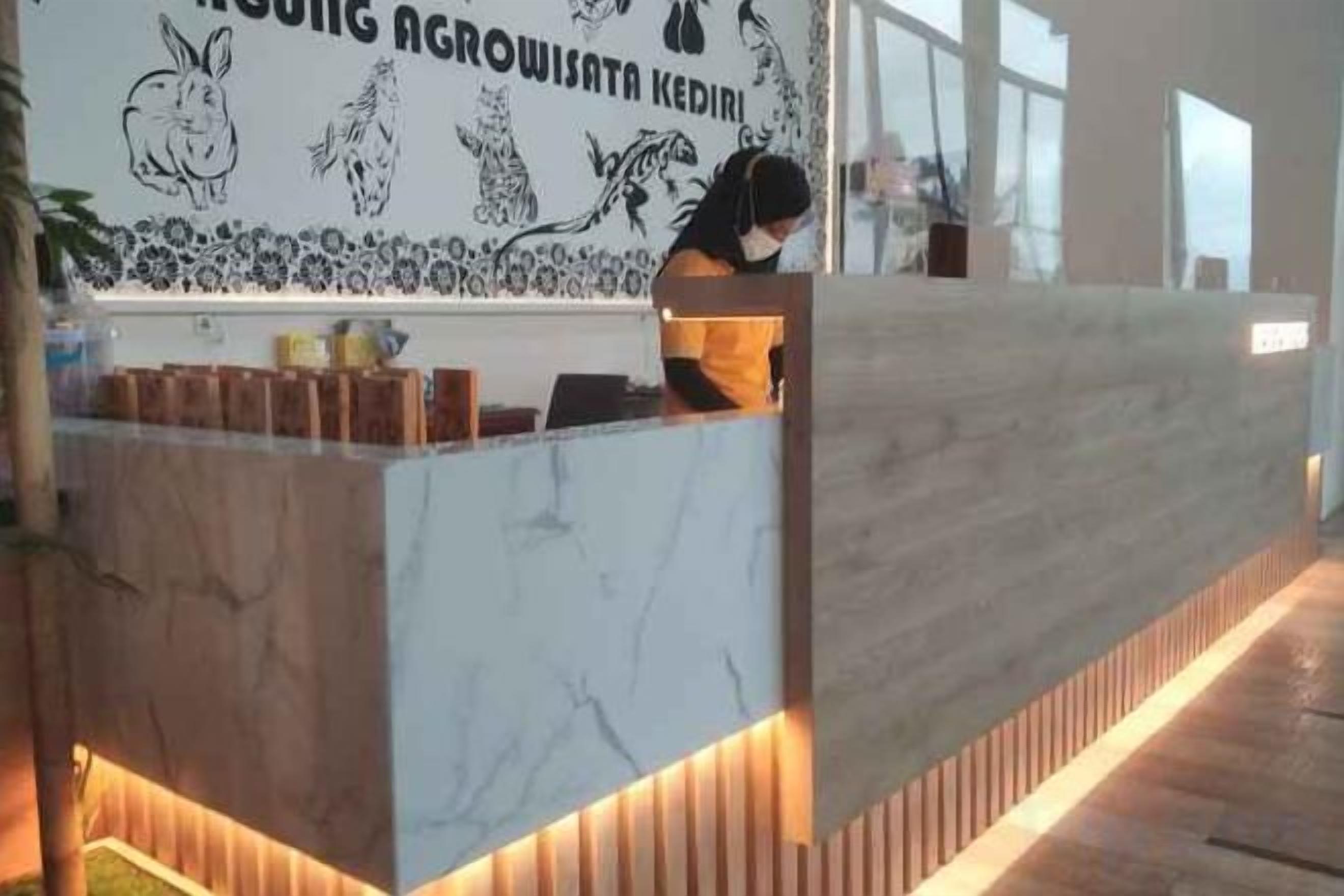 A reception desk with a marble top and wooden accents, a wall with black and white illustrations, and a person standing behind it.