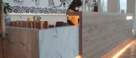 Una recepción con encimera de mármol y detalles de madera, una pared con ilustraciones en blanco y negro, y una persona de pie detrás.