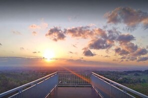 A wooden deck with metal railings overlooking a landscape during sunset.