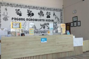 Een receptiebalie met een bloemenmuurdecoratie en een bord met de tekst 'PAGUNG AGROWISATA KEDIRI'.