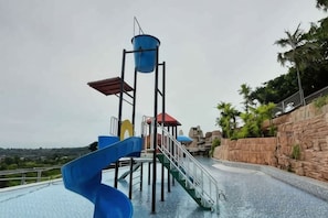 Una estructura de tobogán acuático con diseño en espiral, una plataforma con techo rojo y un tanque de agua cilíndrico azul.