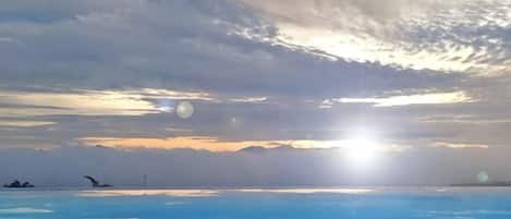 A coastal landscape with a clear sky and the sun setting or rising over the horizon.