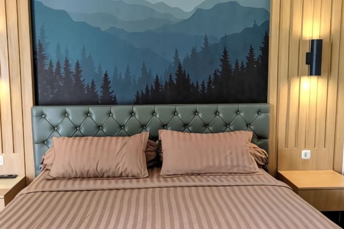 Ein Bett mit einer gebügelten Kopfteil, zwei Kissen, einer gestreiften Bettdecke und einer Wandmalerei von einem Wald.