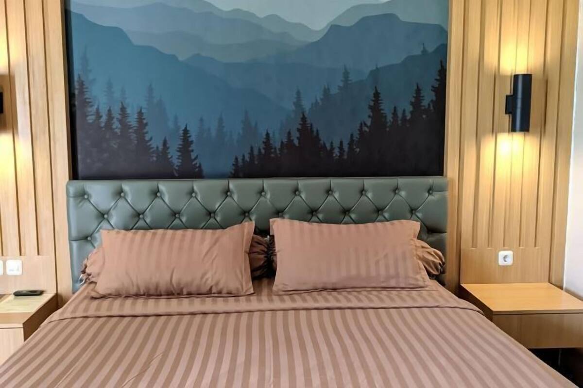 A bedroom with a tufted headboard, two pillows, a striped bedspread, and a wall mural of a forest.