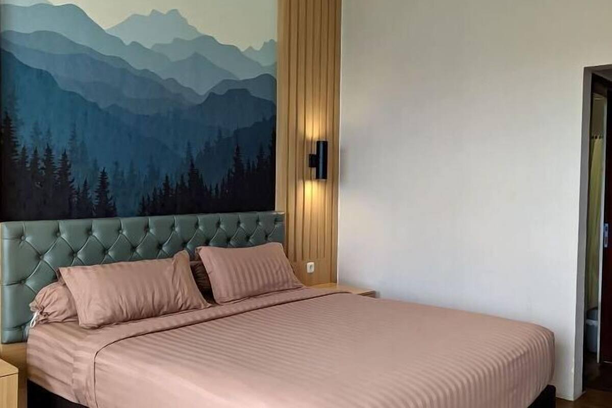 A bedroom with a mountain-themed wall mural, a tufted headboard, and a bed with pink bedding.
