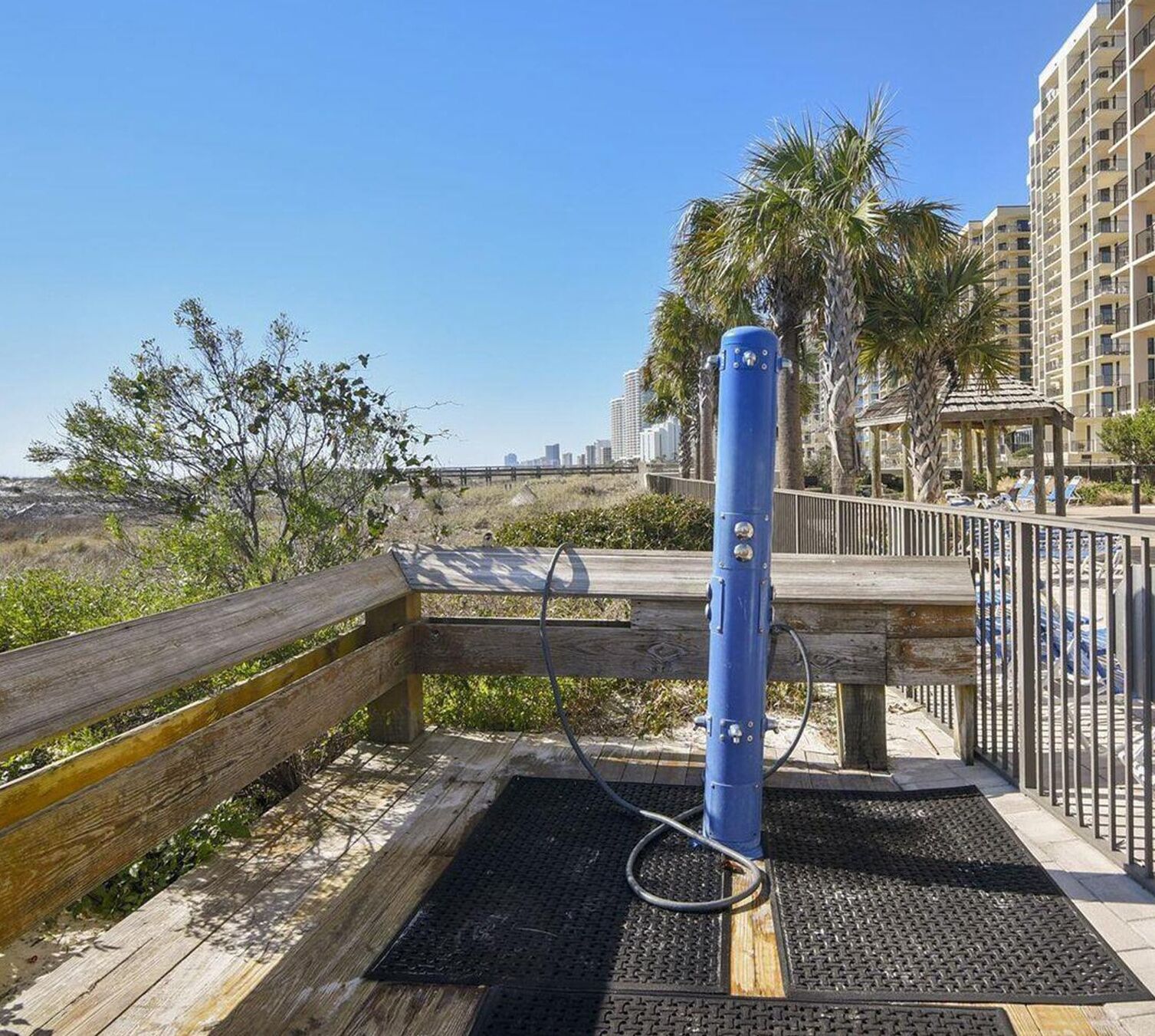 A wooden deck with a blue water feature, a metal fence, and a view of a cityscape in the background.