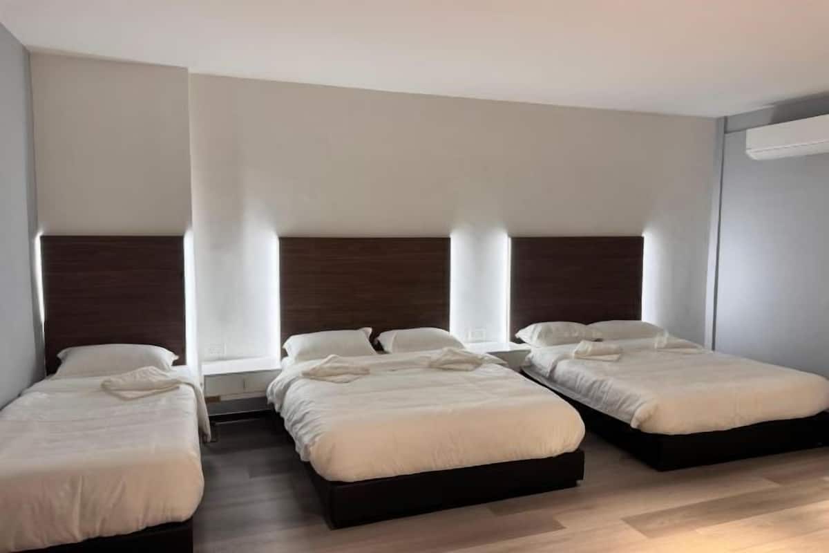 Habitación de hotel con tres camas individuales, un cabecero de madera y un ventanal grande.