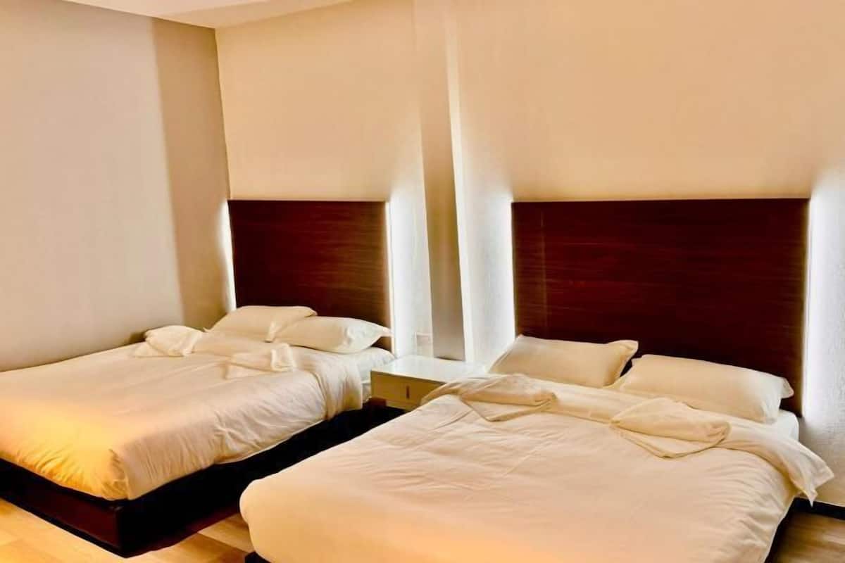 Una habitación de hotel con dos camas individuales, cabecera de madera y una mesita de noche.