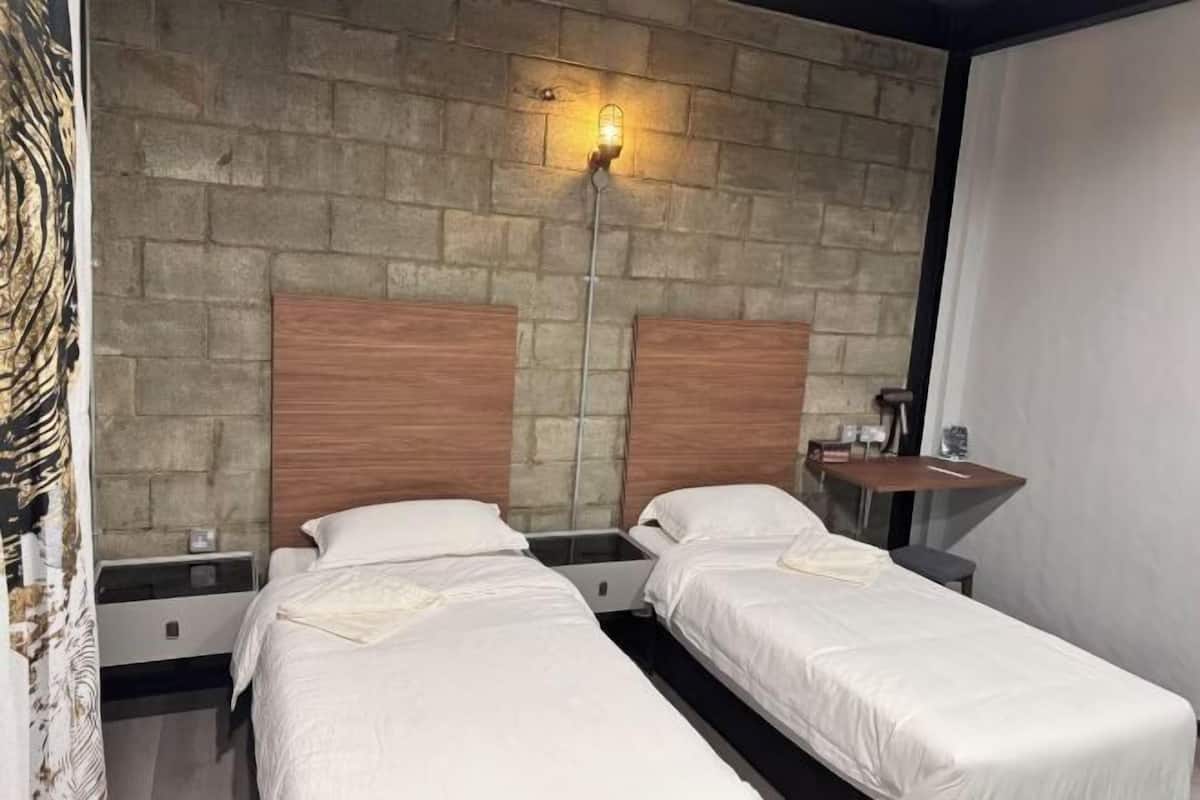 Habitación de hotel con dos camas, una pared de piedra, una mesita de noche y un espejo.
