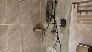 A glass-enclosed shower with a control panel, a handheld showerhead, and a handheld vacuum. - Peaceful Cottage (Semporna)
