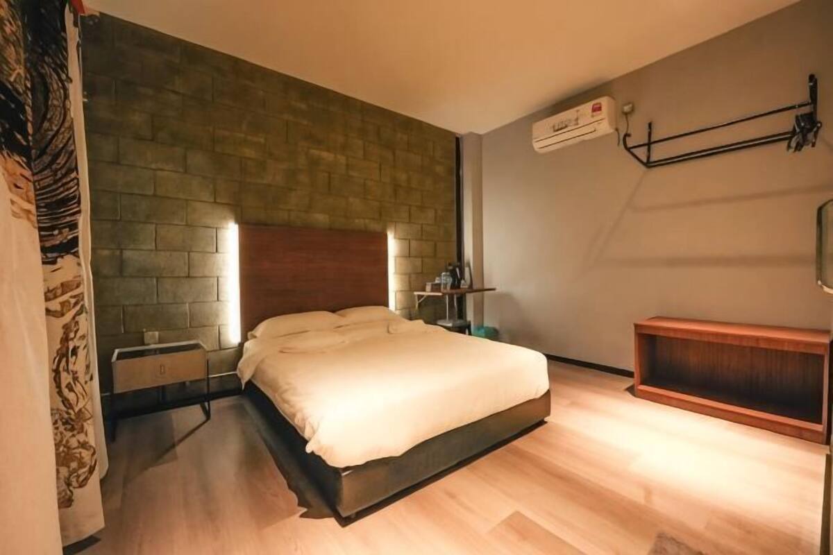 Un dormitorio con pared de ladrillo, cabecero de madera, mesita de noche y un banco de madera.