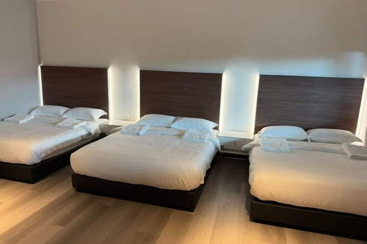Habitación de hotel con tres camas, cabeceros de madera y piso de color claro.