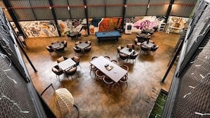 A spacious indoor area with tables and chairs arranged in a circular pattern, a ping pong table, and a mural on the wall. - Peaceful Cottage (Semporna)