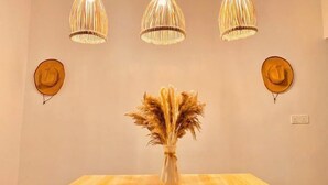 Uma sala de jantar com uma mesa de madeira, três luminárias pendentes e dois chapéus fixados na parede.