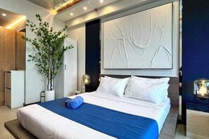 A modern hotel room with a large bed, a potted plant, and a decorative wall piece. - Deluxe Executive End Unit in Downtown Makati (Makati)