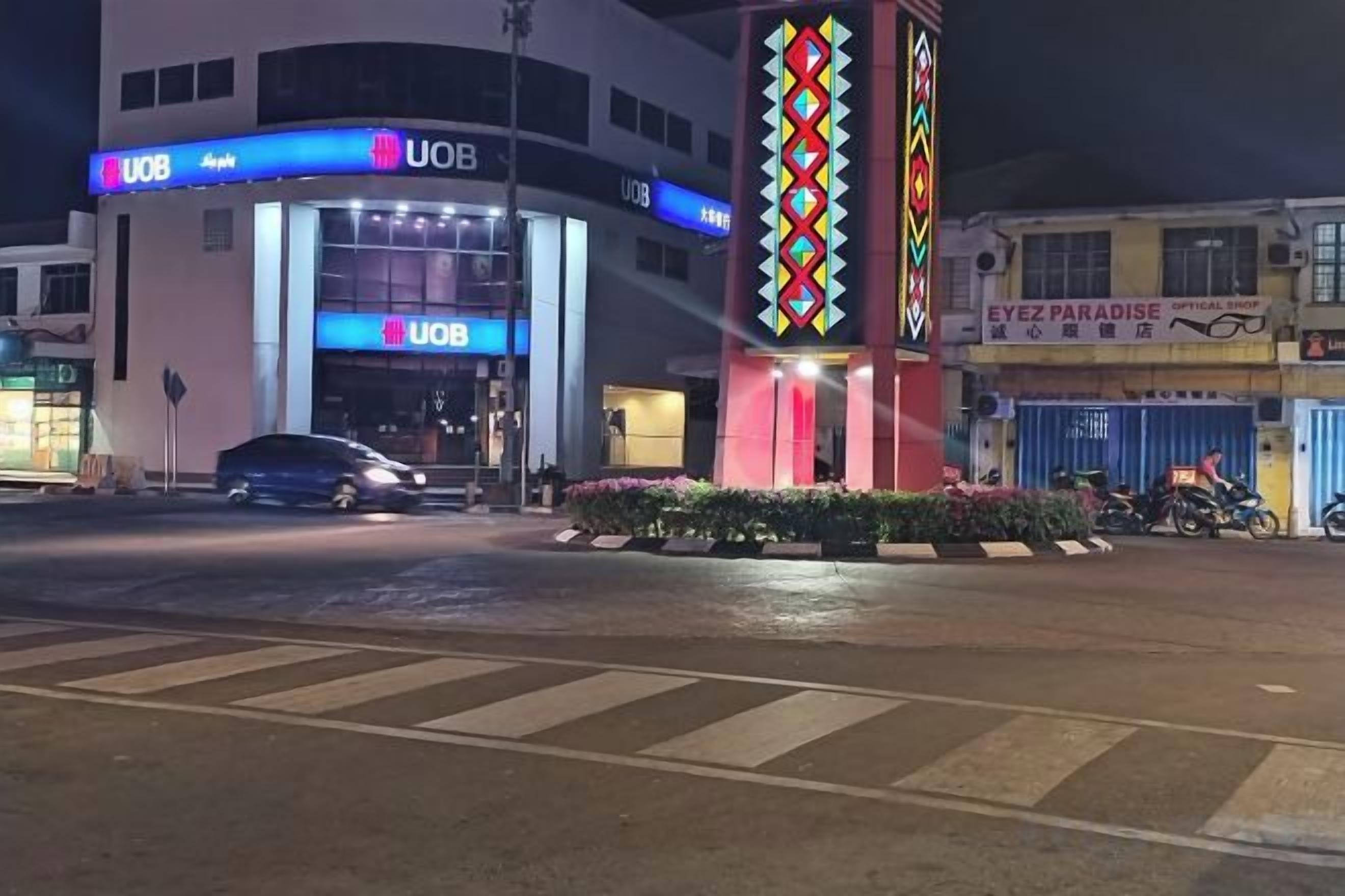 A UOB building with a prominent entrance, a parking area, and a nearby Ez Paradise shop.
