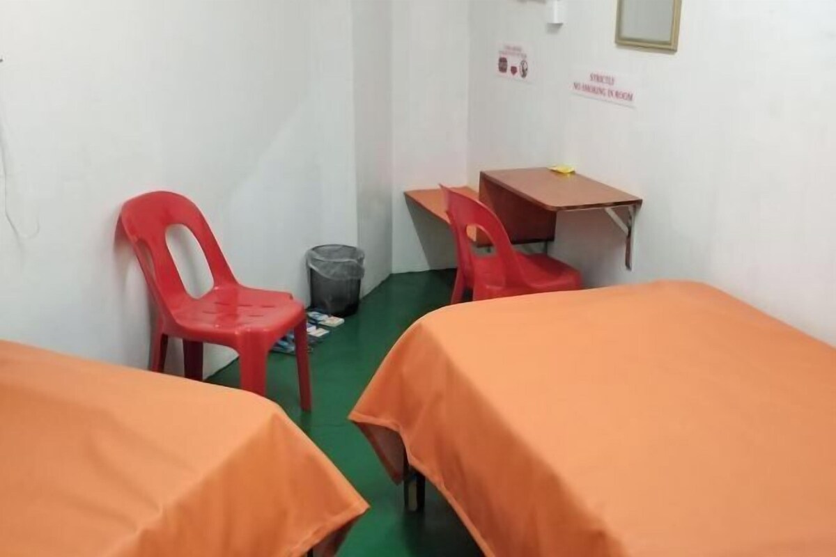 A small, clean room with two beds, a desk, and a chair.