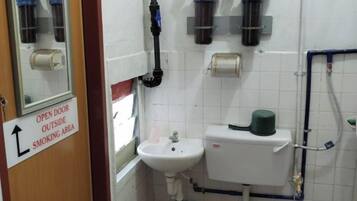 A bathroom with a sink, toilet, and a mirror. There's a sign indicating an open door outside the smoking area.