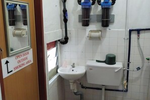 A bathroom with a sink, toilet, and a mirror. There's a sign indicating an open door outside the smoking area.