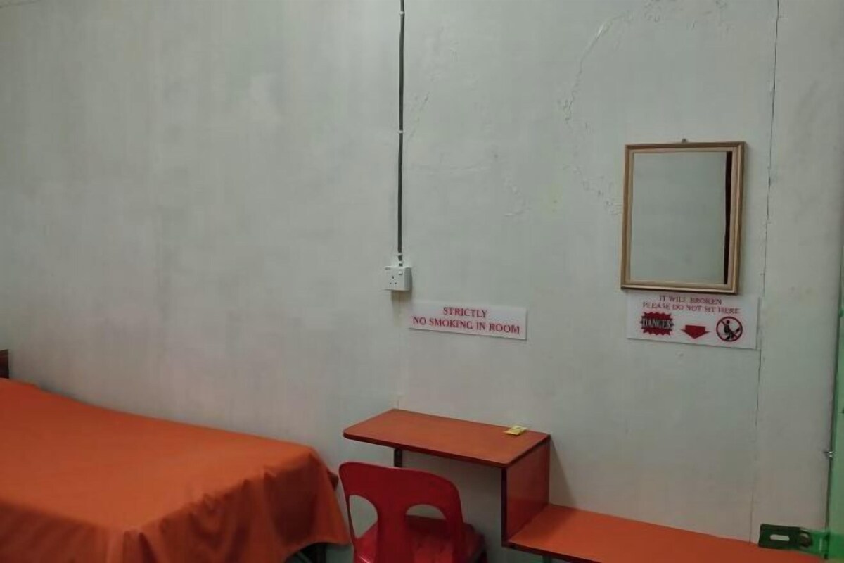 A small room with a bed, a desk, and a chair. There are signs on the wall indicating no smoking and a warning about the mirror.