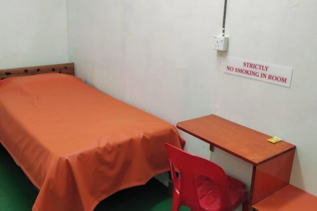 A single-bed room with a 'Strictly No Smoking' sign, a wooden desk, and a red chair.