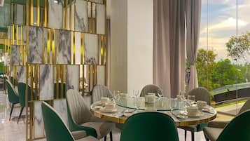 A dining area with a round glass table, green upholstered chairs, and a decorative wall with vertical gold elements and marble panels.