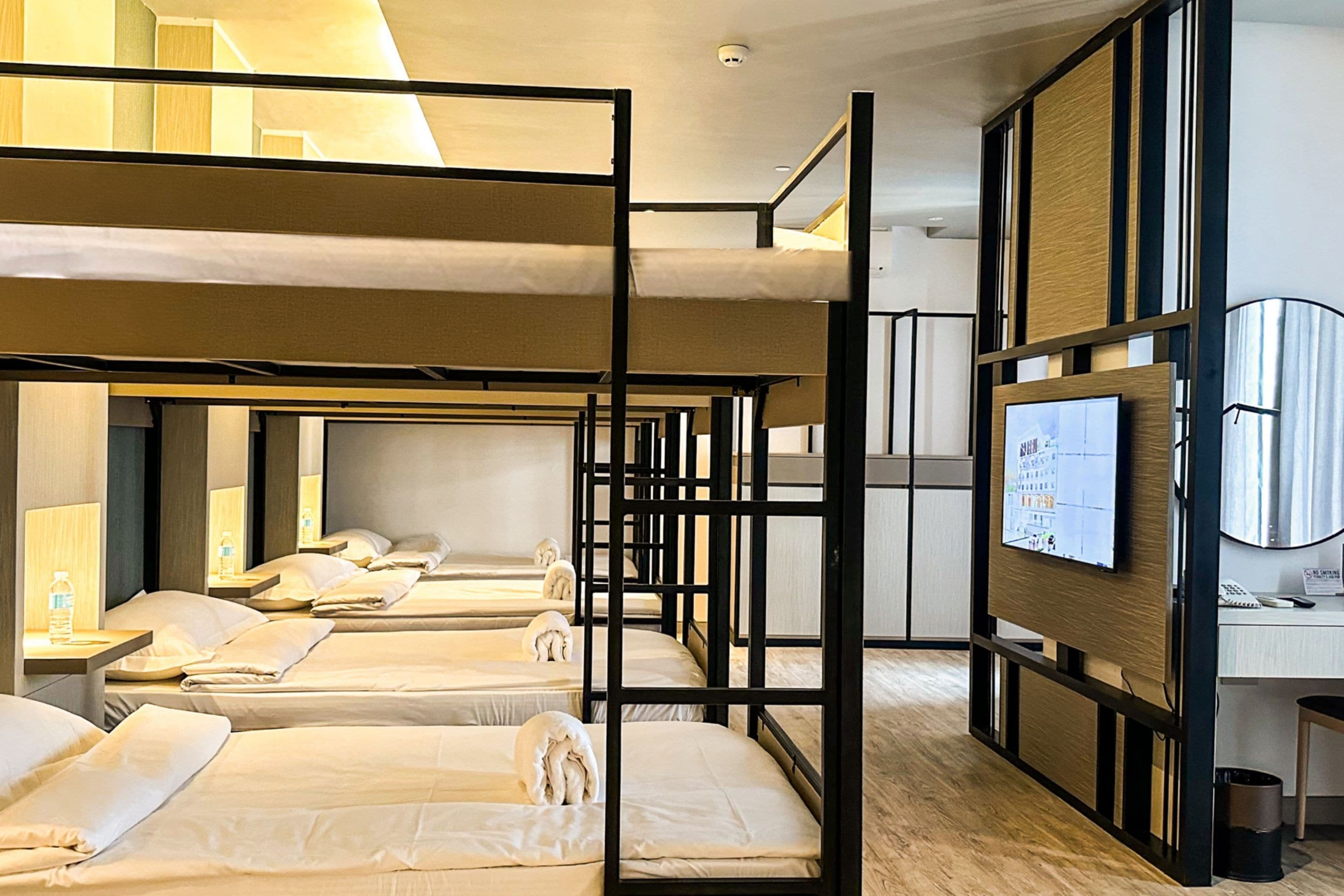 A hotel room with bunk beds, a desk, a television, and a trash bin.