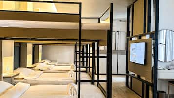 A hotel room with bunk beds, a desk, a television, and a trash bin.