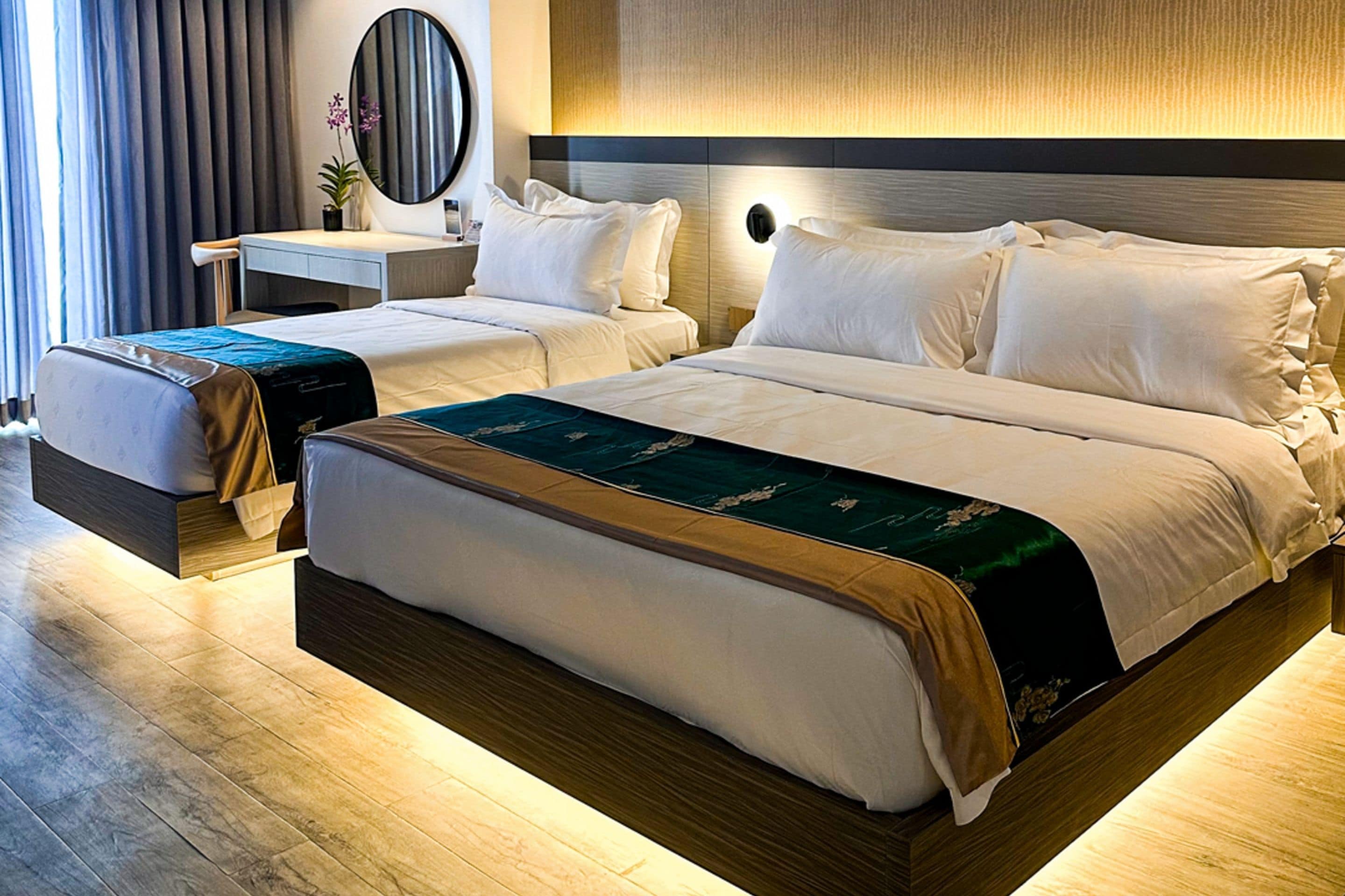 A hotel room with a large bed, a smaller bed, a desk, a mirror, and a nightstand.