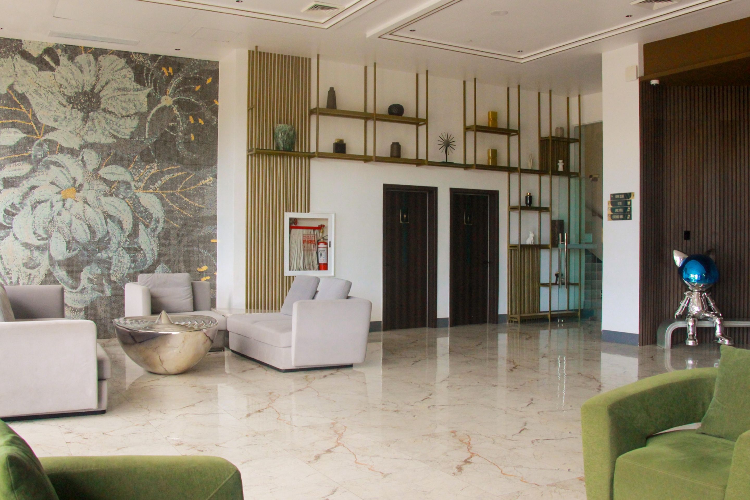 Un vestíbulo amplio con suelo de mármol, un gran mural floral y una estantería moderna con objetos decorativos.