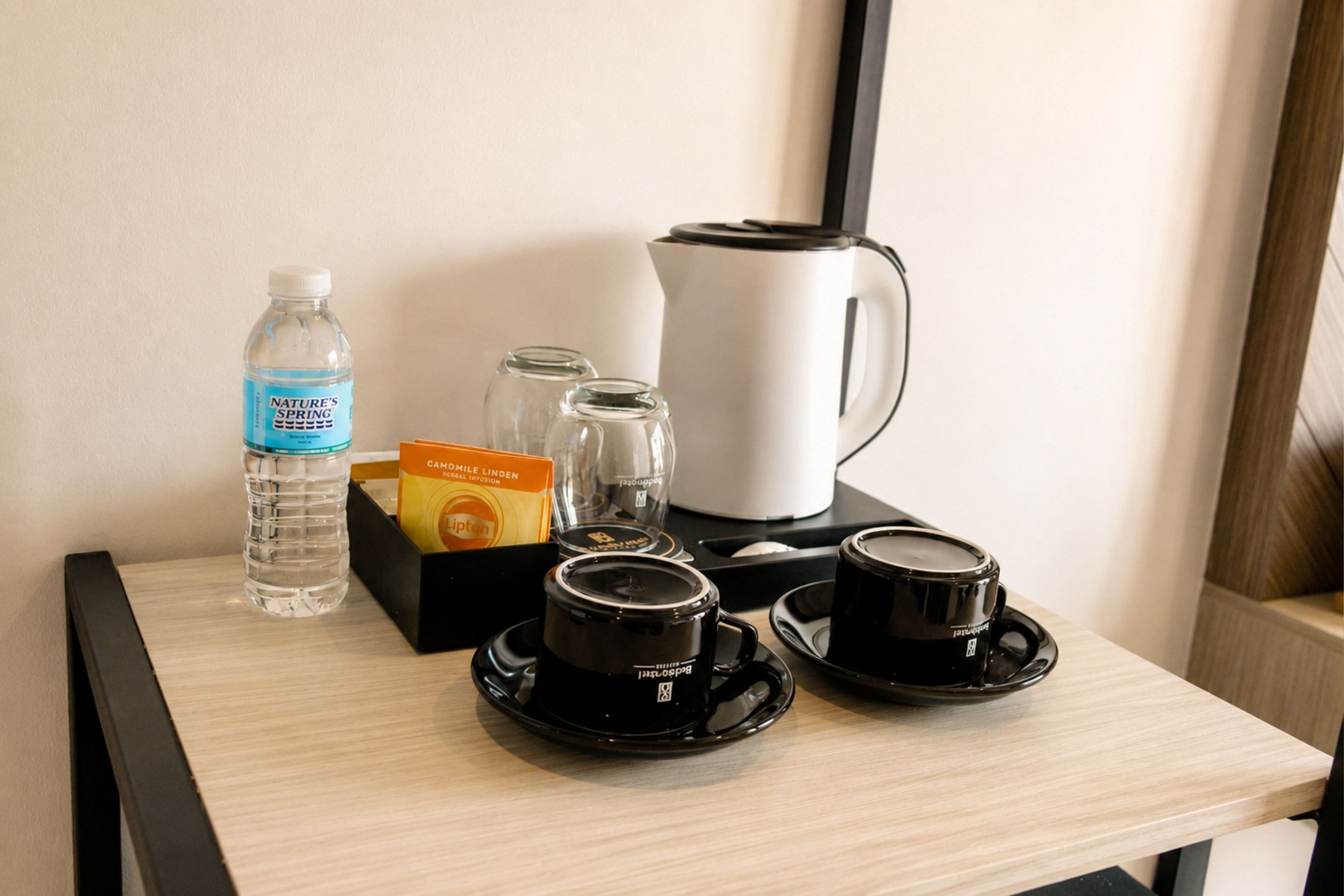 A hotel room's breakfast table with a water bottle, a box of Lipton tea, a coffee maker, and two black coffee cups.