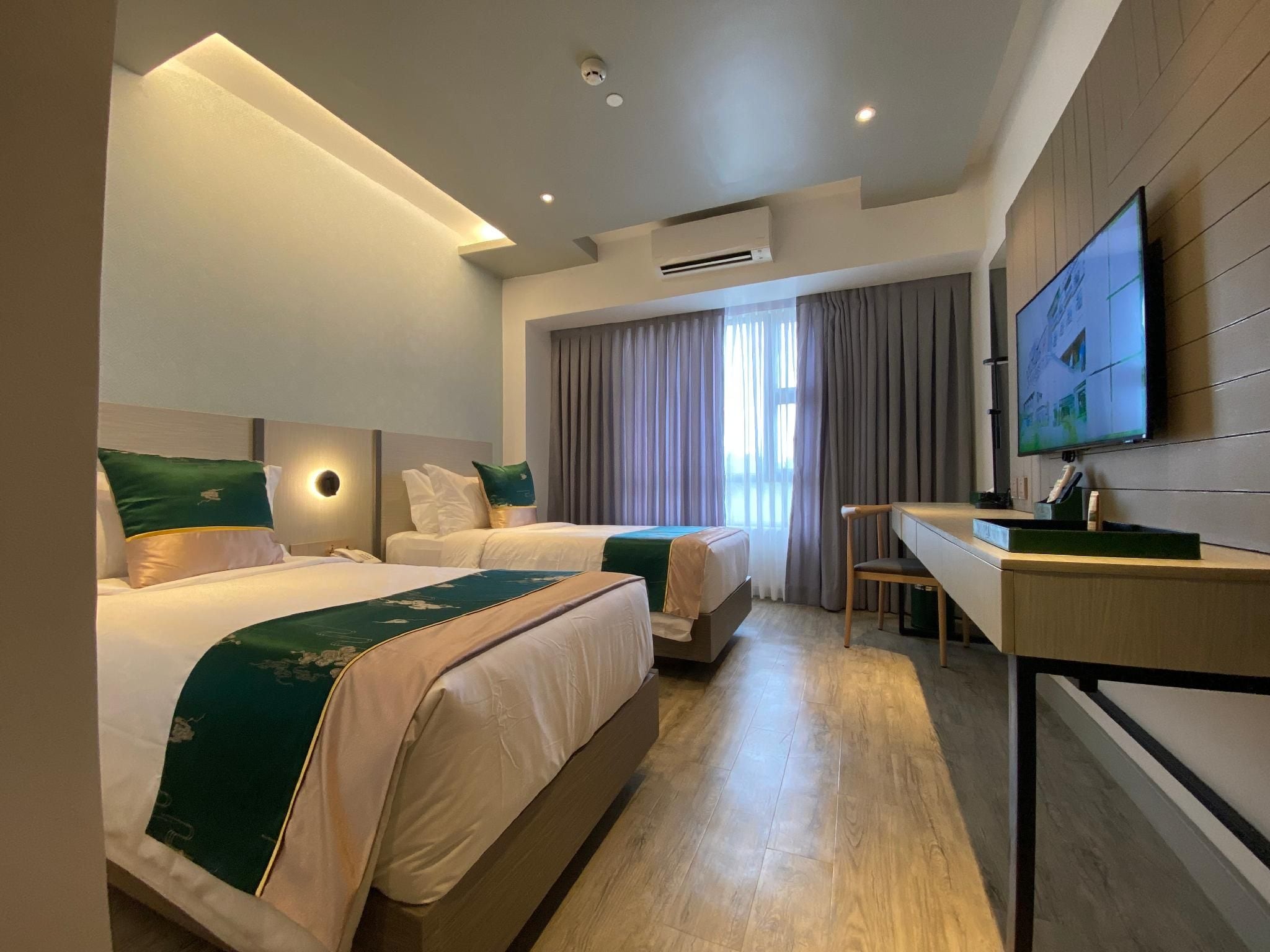 Een hotelkamer met twee bedden, een bureau, een televisie en een groot raam met gordijnen.