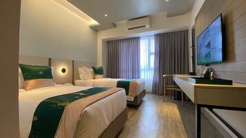 Een hotelkamer met twee bedden, een bureau, een televisie en een groot raam met gordijnen.