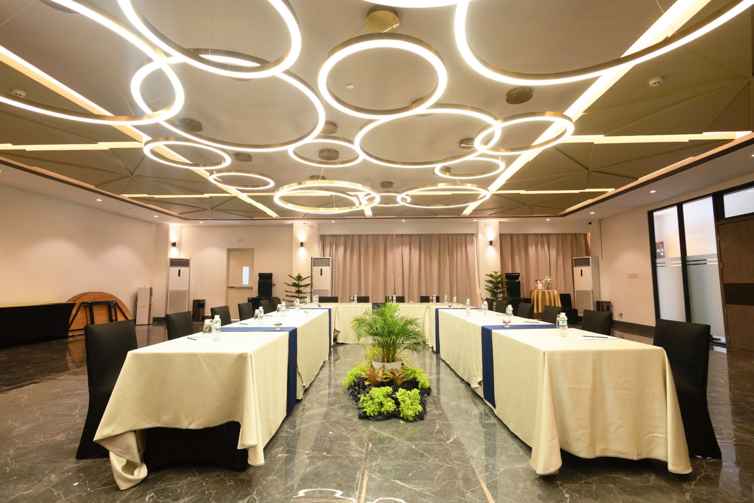 Un salón de conferencias con una larga mesa, sillas e iluminado por lámparas circulares en el techo.