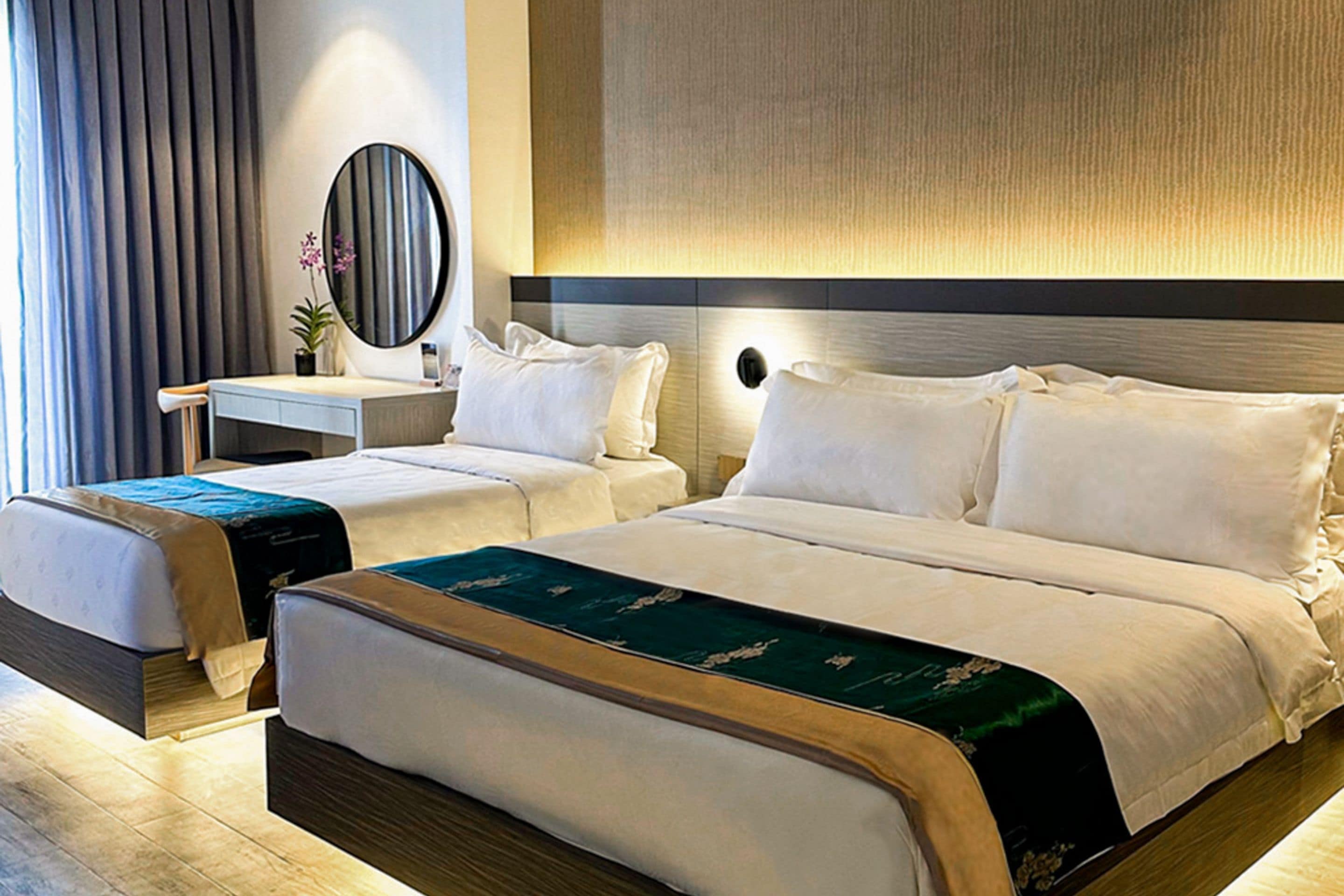 A hotel room with a large bed, a smaller bed, a desk, and a mirror.