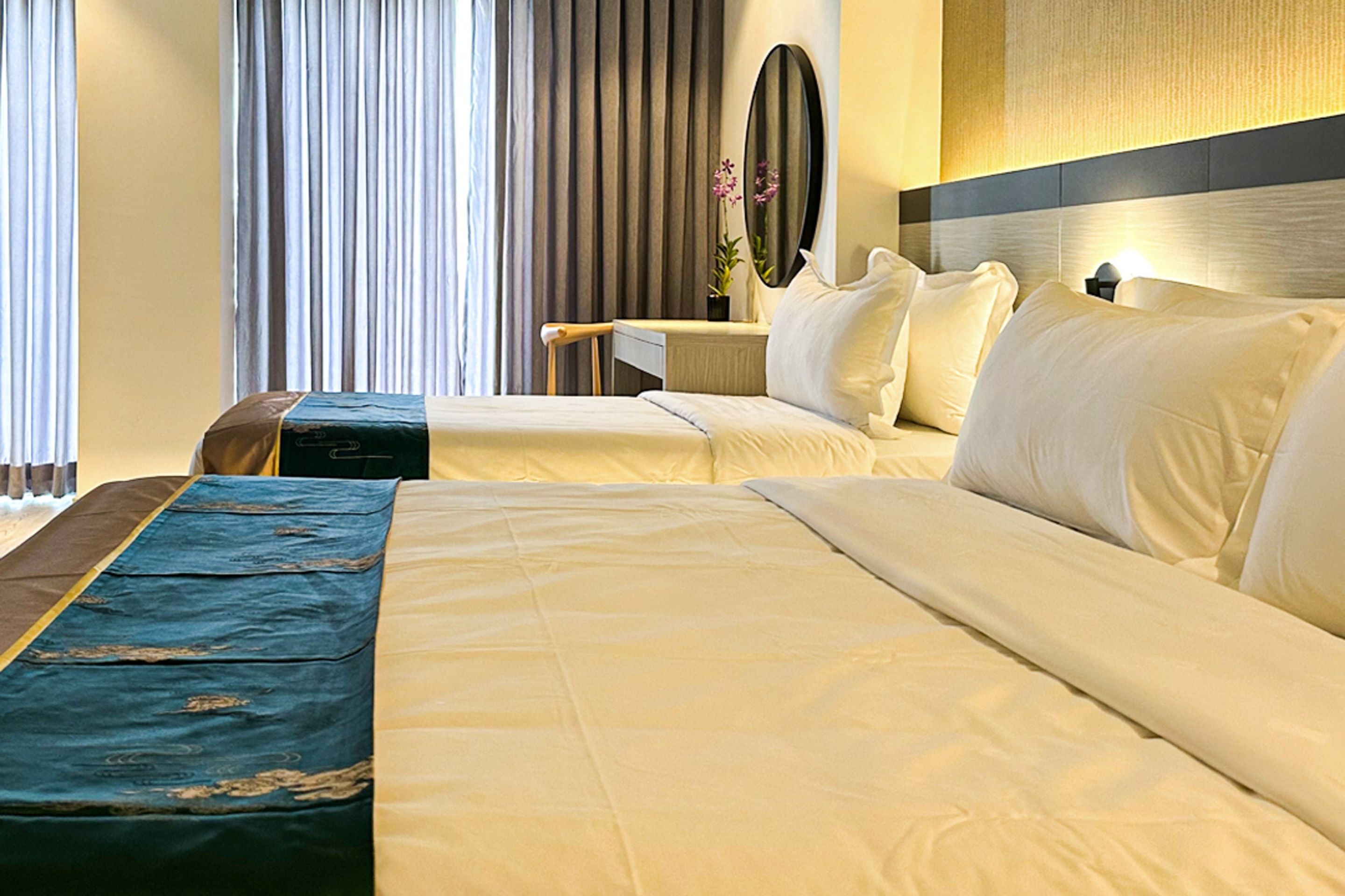 A hotel room with two beds, a desk, a chair, a mirror, and a window with curtains.