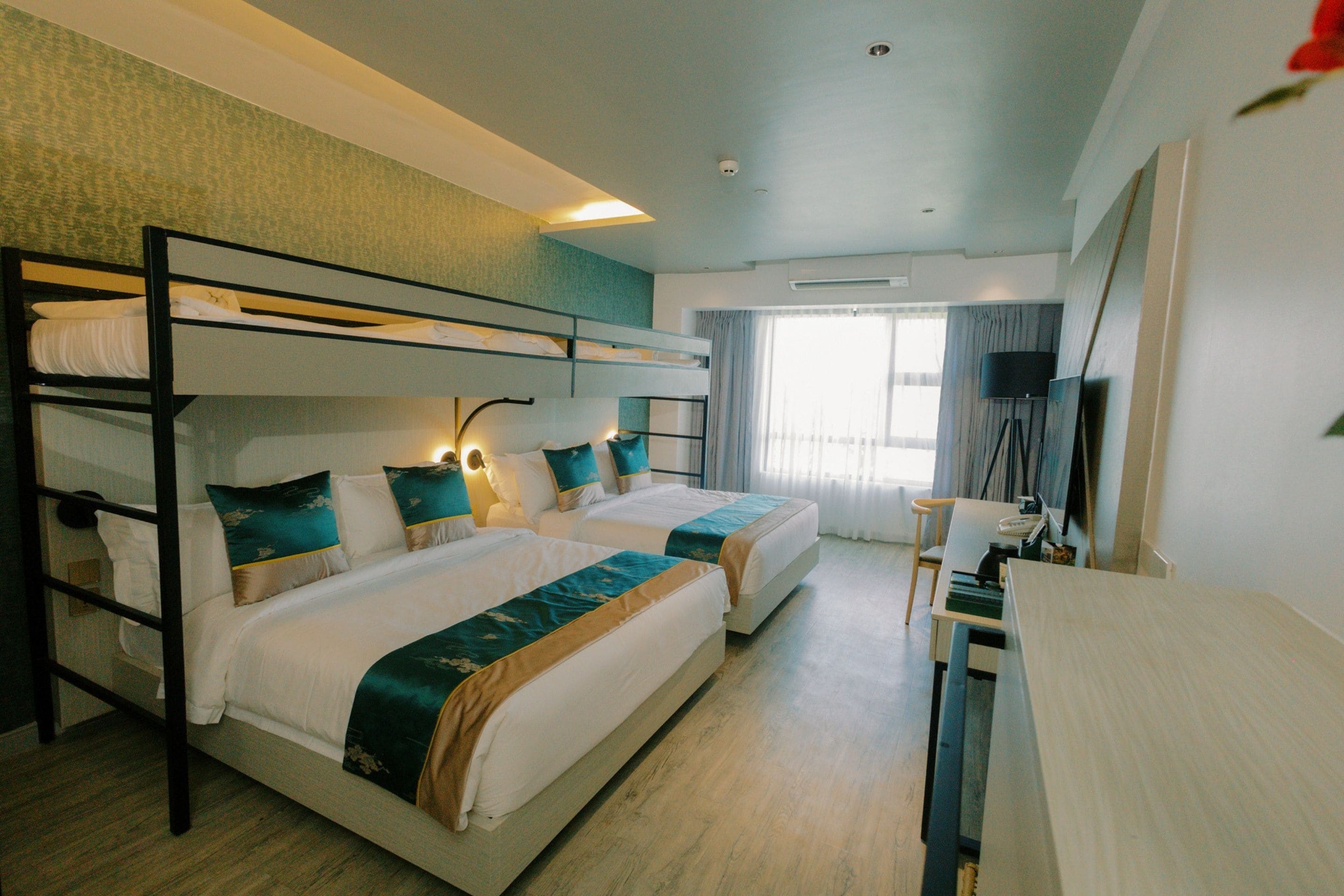 Habitación de hotel con literas, un escritorio, una silla, un televisor y una ventana con cortinas.