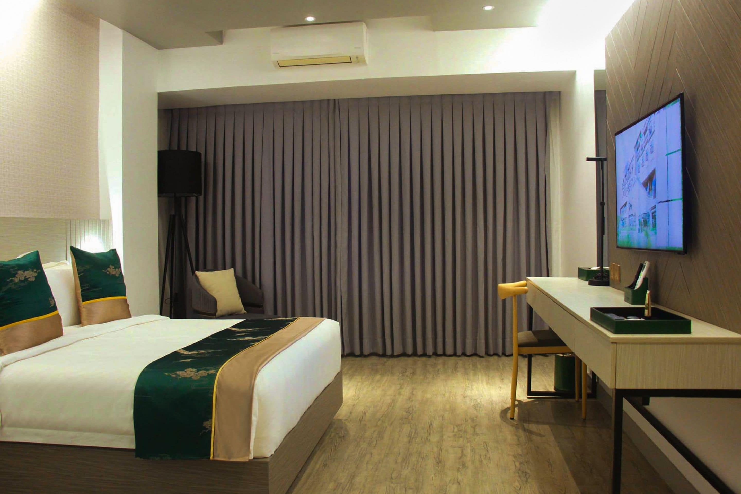 A hotel room with a bed, a desk, a television, and a window with curtains.